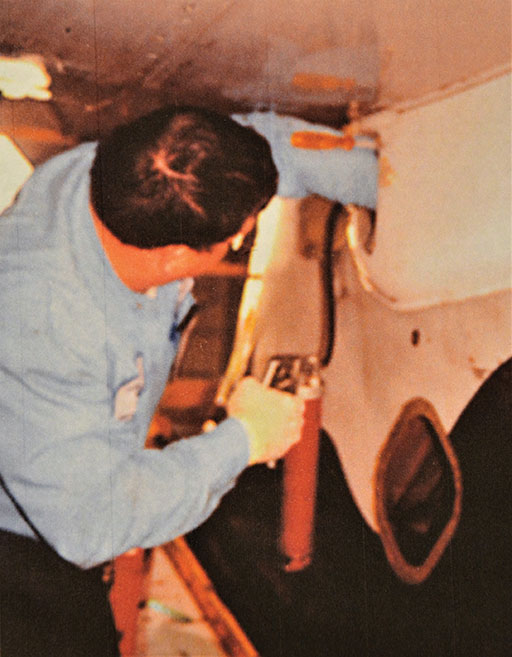 Image 11: A mechanic on a tail stand demonstrates the use of a grease gun, through a small access panel, to pump grease into the single fitting of the acme nut on an actual MD-80 series airplane.
