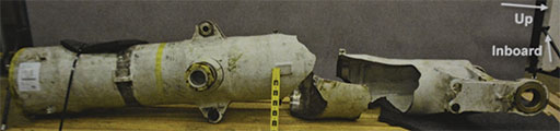 Photo 9. View of the fractured left main landing gear cylinder after NTSB metallurgists laid out the fractured pieces for review.