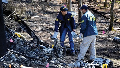 Graphic 7. NTSB Investigators Chihoon Shin (left) and Luke Schiada survey the damage of a helicopter accident that occurred in Pigeon Forge, Tenn.